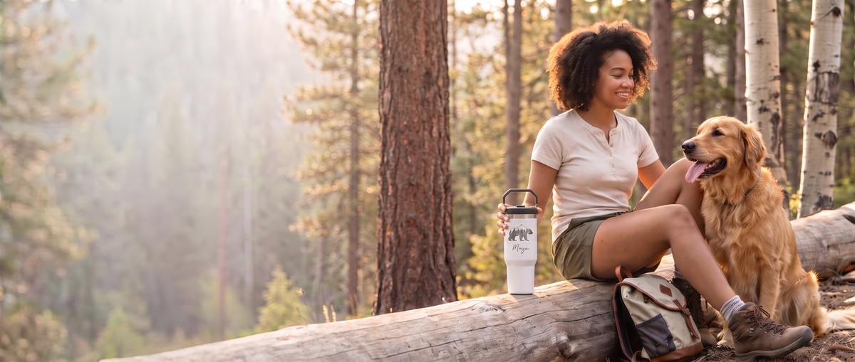 Woman resting during a forest hike with her golden retriever, holding a personalized laser-engraved white Stanley IceFlow tumbler